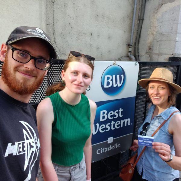 Trois militants se prennent en photo devant la plaque d'un hôtel. Une militante tient un petit tract dans sa main.